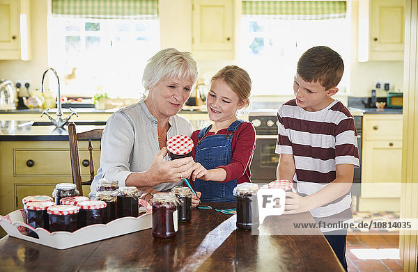 Grandmother canning jam with grandchildren in kitchen