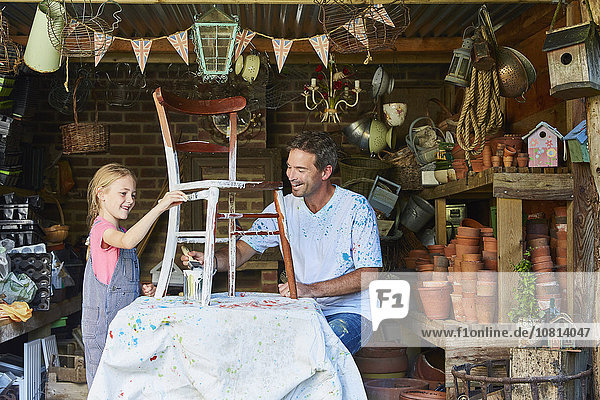 Father and daughter painting chair in workshop