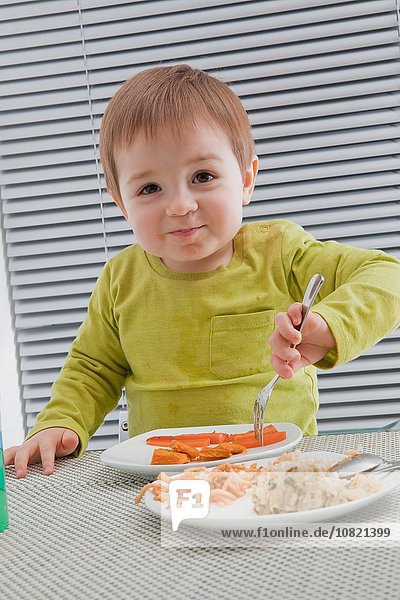 Baby Junge füttert sich selbst am Esstisch