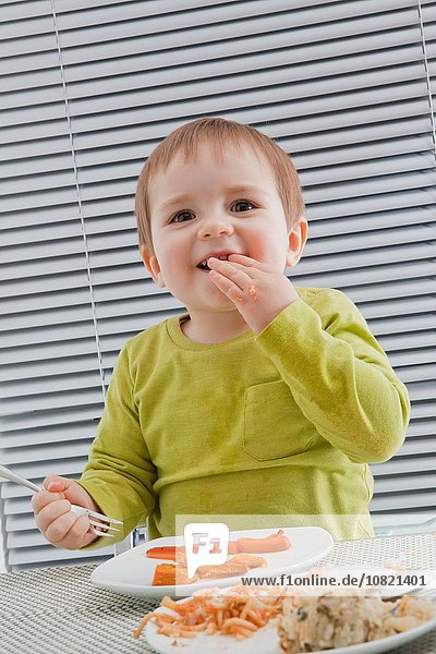 Baby Junge füttert sich selbst am Esstisch