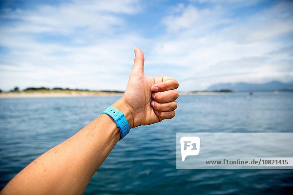 Female hand giving thumbs up over Nehalem Bay  Oregon  USA