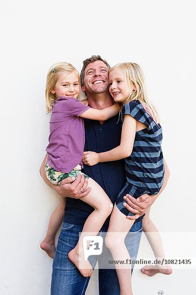 Portrait of mature man carrying two young daughters in front of white wall