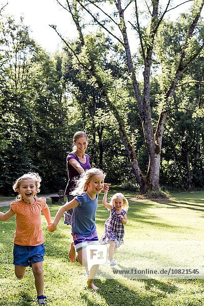 Mid adult woman running and holding hands with three daughters in park