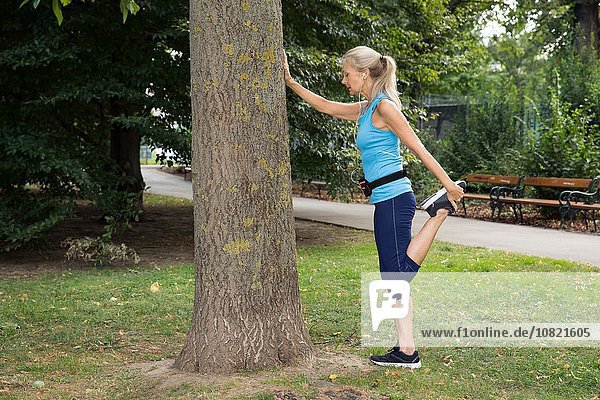 Reife Frau streckt das Bein während des Trainings im Park