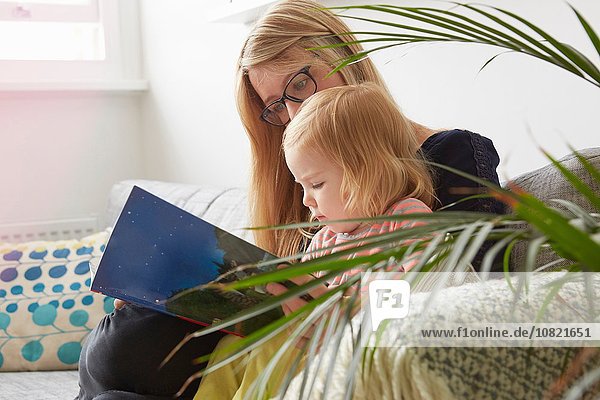 Mittlere erwachsene Frau und Kleinkind Tochter lesen auf dem Wohnzimmersofa