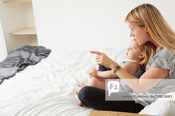 Mid adult woman sitting with toddler daughter on bed