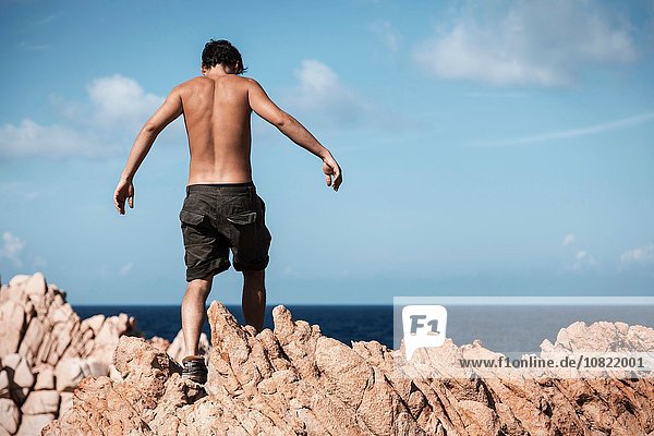Nackter junger Mann in Khaki-Shorts über Felsen kletternd  Costa Smeralda  Sardinien  Italien
