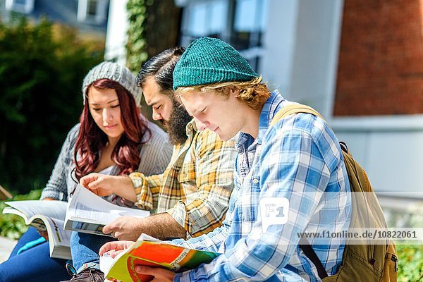 Drei erwachsene Studenten beim Lesen von Büchern an der Campuswand