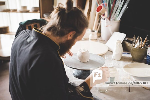 Rückansicht des erwachsenen Mannes in der Werkstatt beim Auftragen der Keramikglasur auf den Tontopf
