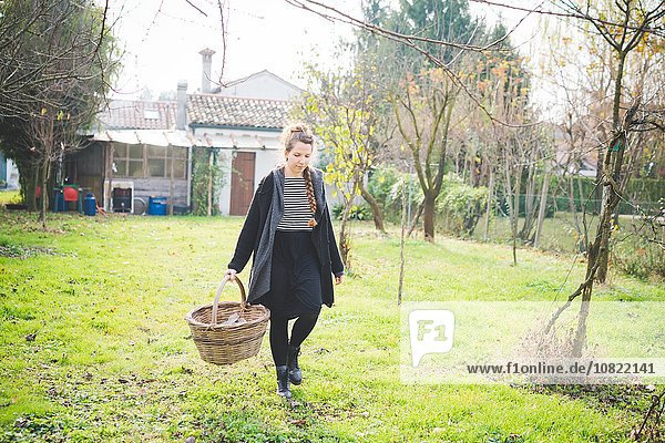 Durchgehende Vorderansicht der jungen Frau im Garten mit Weidenkorb