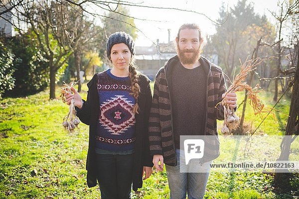 Ein Paar steht im Garten und hält frische Knoblauchzwiebeln in der Hand.