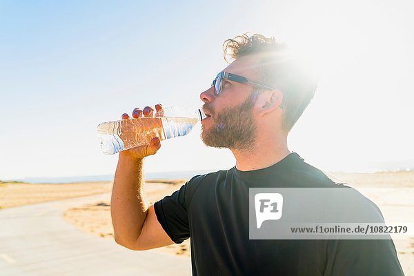 Young man  by beach  drinking from water bottle