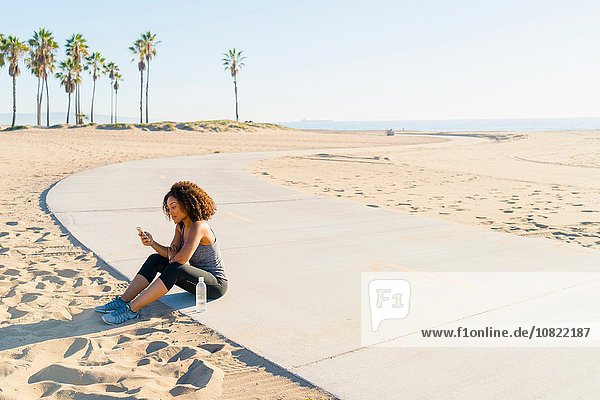 Mittlere erwachsene Frau am Strand sitzend  mit Smartphone