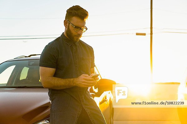 Young man leaning against car  using smartphone