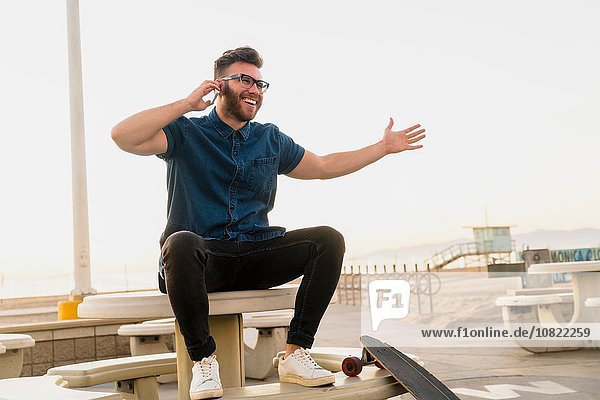 Junger Mann im Freien sitzend  mit Smartphone  lachend