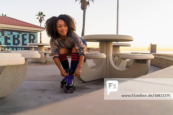 Mid adult woman sitting outdoors  tying rollerskates