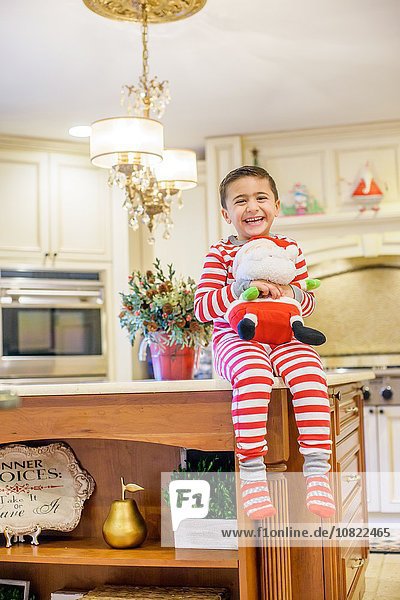 Porträt eines Jungen  der auf der Küchenzeile sitzt und Weihnachtsmann hält.