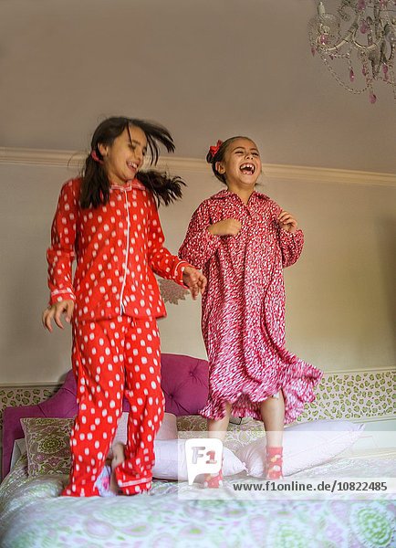 Zwei glückliche Schwestern springen auf dem Bett.