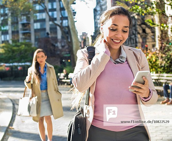 Junge Frau liest Smartphone-Texte beim Spaziergang durch den Stadtpark
