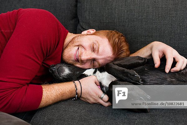 Junger Mann auf dem Sofa liegend umarmend Hundeaugen geschlossen lächelnd