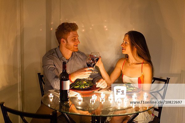 Paar am Tisch von Angesicht zu Angesicht bei Kerzenlicht essen  einen Toast aussprechen  lächeln