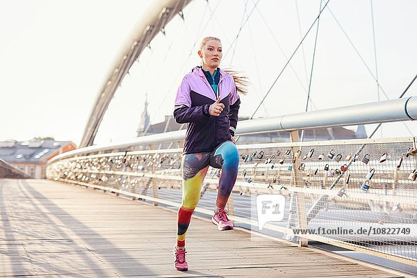 Mid adult female runner running at speed on city footbridge