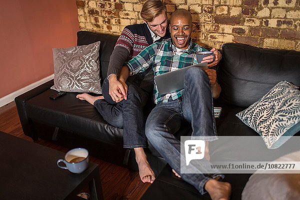 Männliches Paar  das sich zusammen auf dem Sofa entspannt und auf den Laptop schaut.