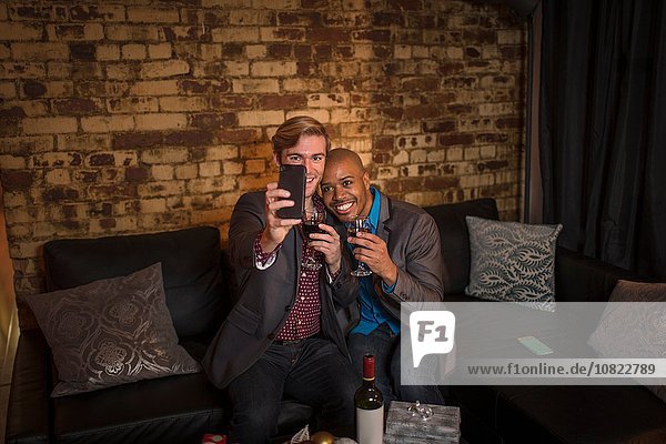 Männliches Paar auf Sofa sitzend  Selbstporträt mit dem Smartphone aufnehmend
