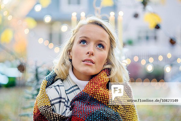 Porträt der jungen Frau in Decke gehüllt vor Weihnachtsbeleuchtung