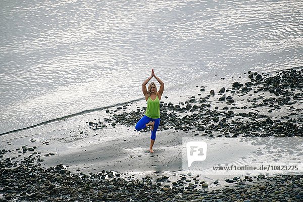 Junge Frau praktiziert Yoga stehend Baum Pose am Strand