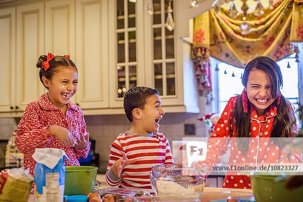 Kinder im Pyjama beim Backen in der Küche,  lachend