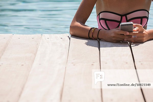Cropped Schuss des Mädchens im Schwimmbad mit Smartphone