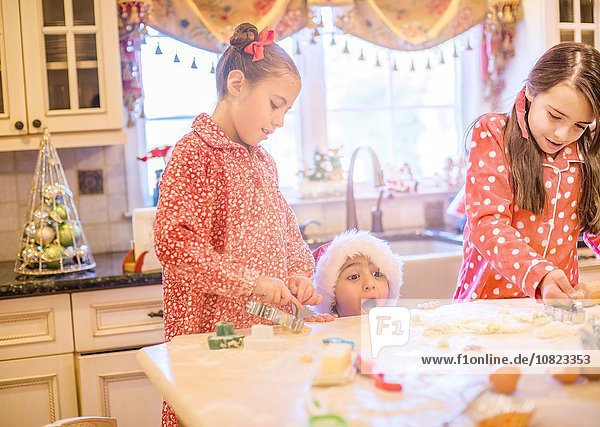 Junge in der Küche mit Nikolaushut  der Kekse mit Schwestern macht  die über die Küchentheke schauen.