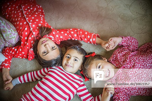 Overhead-Ansicht von Kindern im Pyjama  die auf einem Teppich liegen und lächelnd in die Kamera schauen.