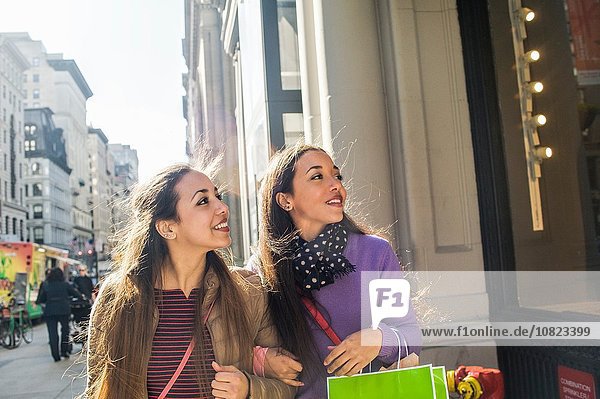 Young female adult twins with shopping bags looking up at shop window