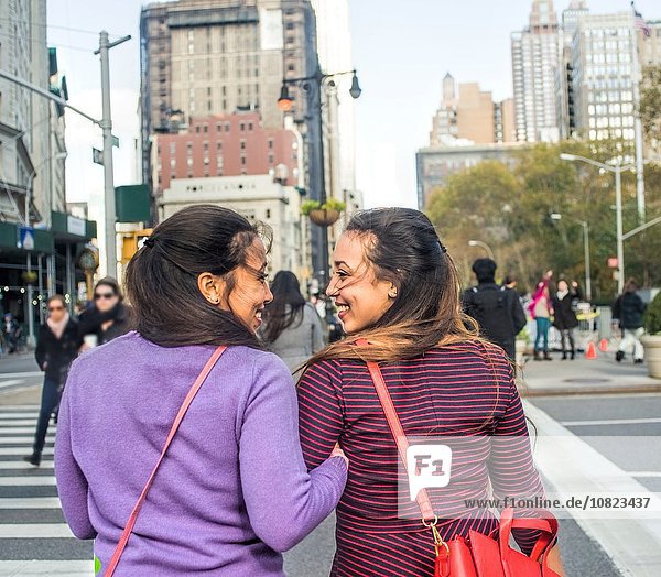 Rückansicht der jungen weiblichen erwachsenen Zwillinge Arm in Arm über die Stadtstraße