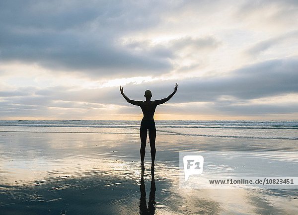 Silhouette of person raising arms on beach
