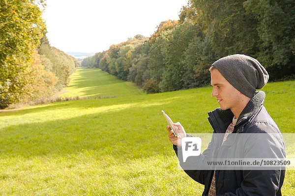 Junger Mann im Feld beim Lesen von Smartphone-Texten  Great Missenden  Buckinghamshire  U.K.