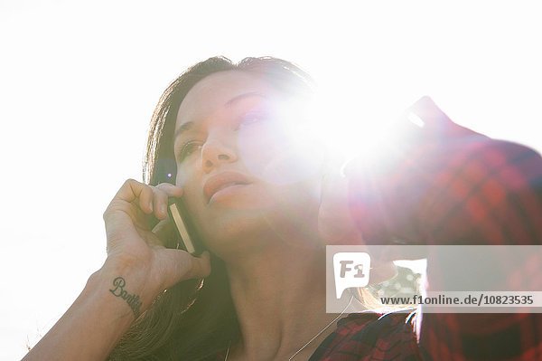 Junge Frau spricht auf dem Smartphone gegen den sonnigen Himmel
