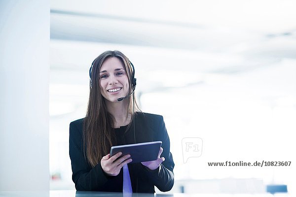 Junge Frau mit Telefon-Headset mit digitalem Tablett und lächelndem Blick auf die Kamera