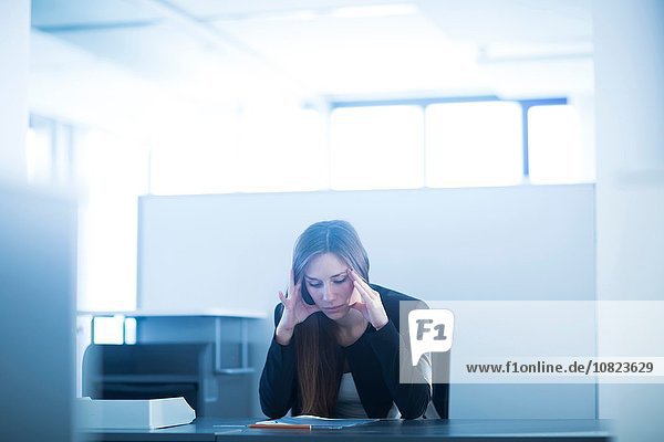 Junge Frau sitzt am Schreibtisch im Büro  Kopf in den Händen schaut nach unten  gestresst