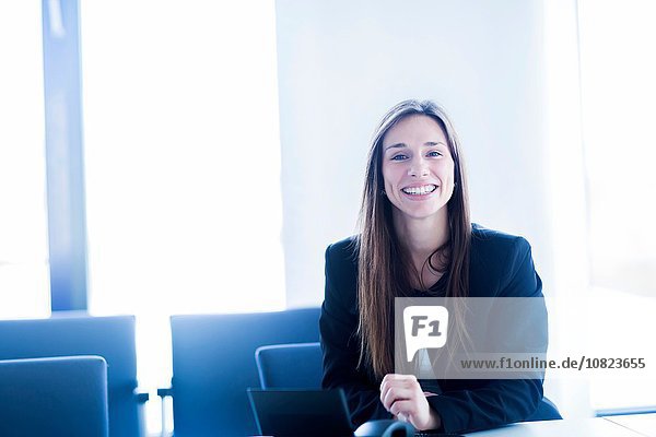 Junge Frau mit digitalem Tablett sitzend vor der Kamera lächelnd