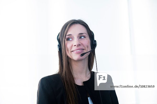 Junge Frau mit Telefon-Headset schaut lächelnd weg