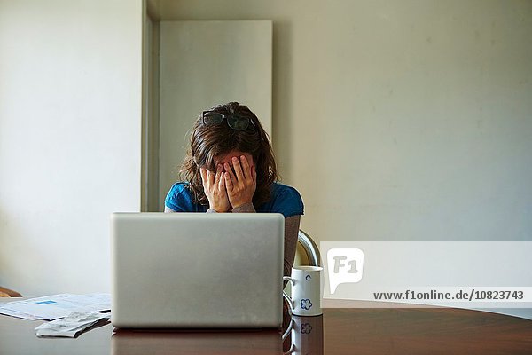 Junge Frau am Tisch sitzend mit Laptop,  sieht gestresst aus