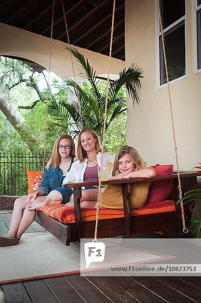 Mutter mit Töchtern  auf der Veranda sitzend  mit lächelndem Blick auf die Kamera.