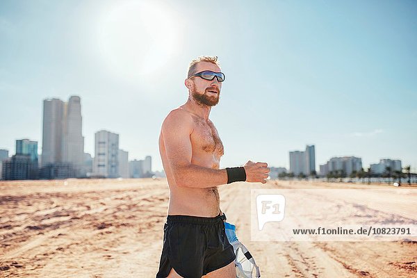 Barechested man on sand wearing sunglasses by skyscrapers  Dubai  Vereinigte Arabische Emirate