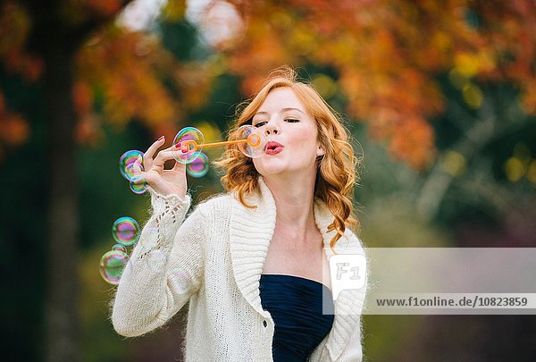 Young beautiful woman with red wavy hair blowing bubbles in autumn forest