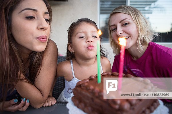 Young girl sitting with family  blowing out candles on birthday cake
