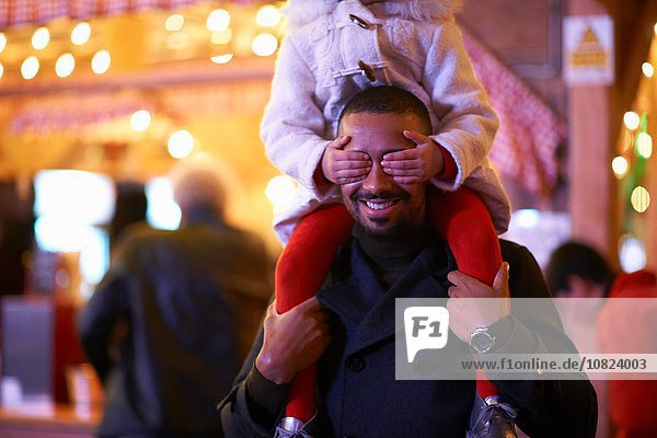 Father carrying daughter on shoulders  daughter covering father's eyes