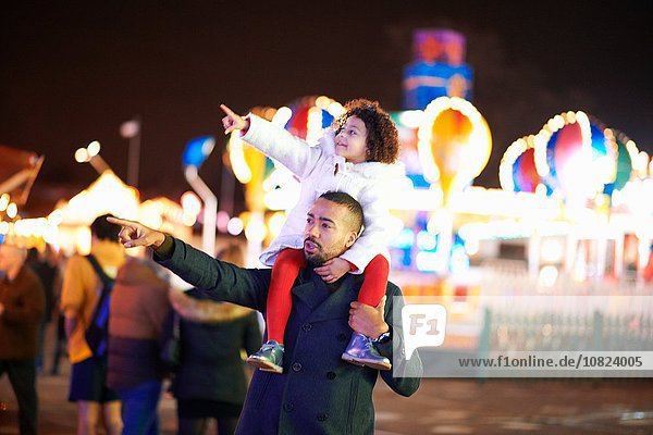 Father carrying daughter on shoulders at funfair  father and daughter pointing